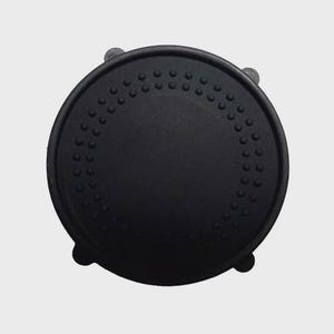 May include: A black, circular object with a textured surface and a series of small, raised dots around the edge. The object has a slightly domed shape and appears to be made of a matte material. Four small, rounded protrusions are visible on the underside.