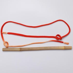 May include: A red and orange rope tied to a wooden stick. The rope is tied in a knot and the ends of the rope are frayed.