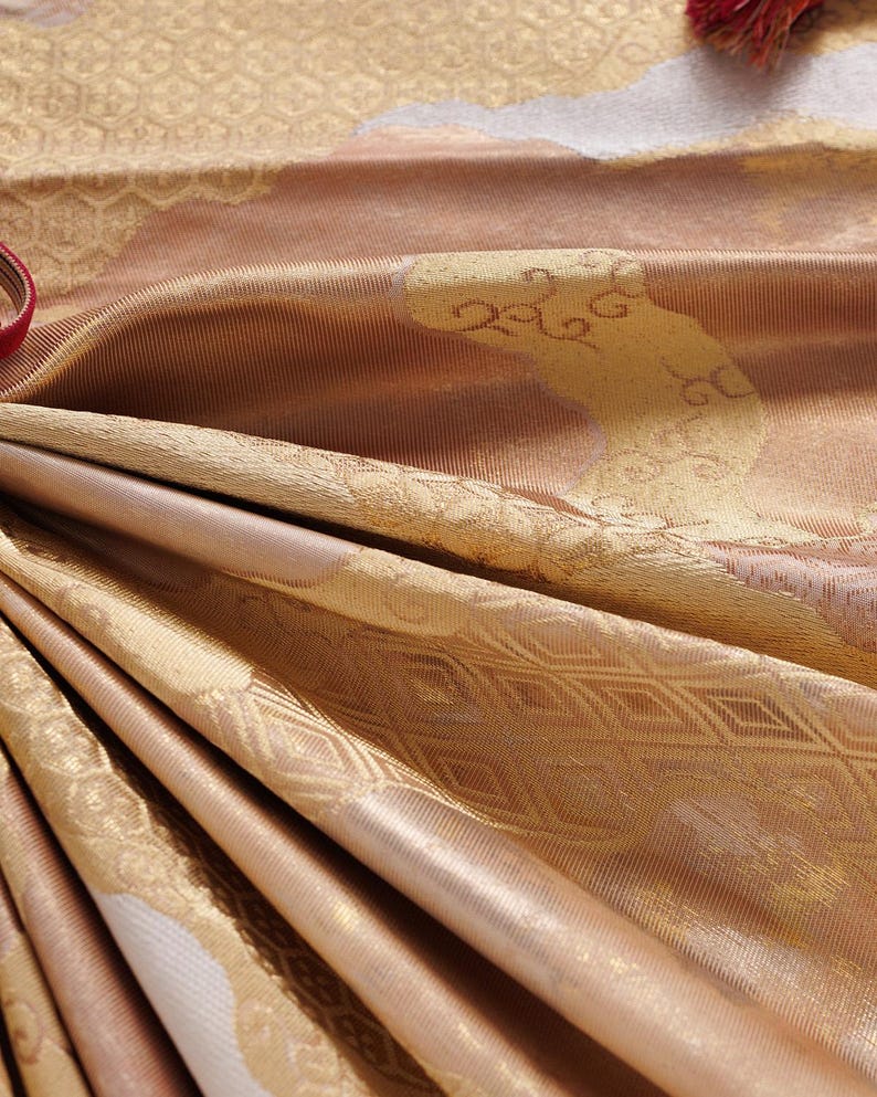 May include: Close-up of a gold and brown fabric with a textured pattern. The fabric has a subtle sheen and a soft, luxurious feel.