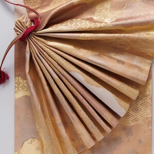May include: A close-up of a folded piece of fabric with a gold and brown pattern. The fabric is tied with a red ribbon.