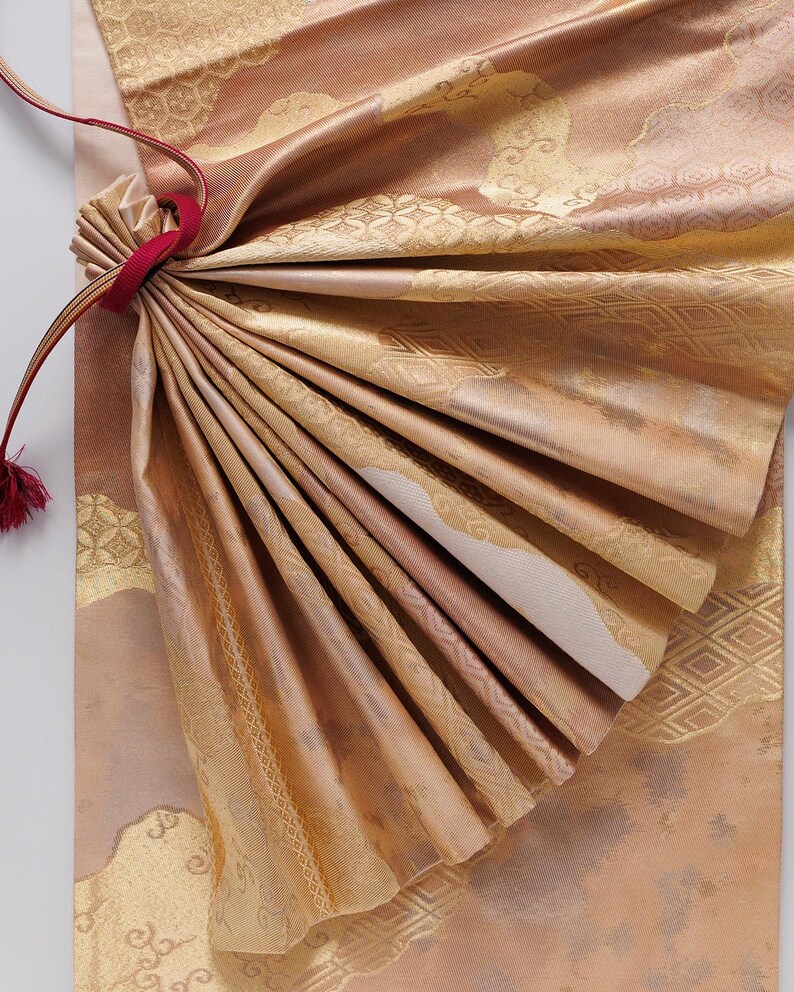 May include: A close-up of a folded piece of fabric with a gold and brown pattern. The fabric is tied with a red ribbon.