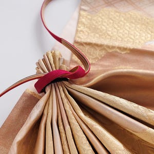 May include: A gold and pink fabric bag with a red drawstring. The bag is folded and has a textured pattern.