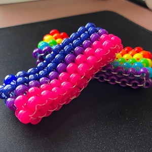 May include: Two colorful beaded bracelets, one with a rainbow pattern and the other with a pink, purple, and blue gradient.