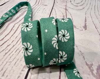 May include: A close-up of three rolls of green fabric ribbon with a white and black swirl pattern.