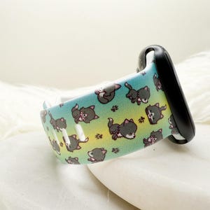 May include: A silicone watch band featuring a gradient background transitioning from teal to yellow, decorated with a repeating pattern of small gray cartoon wolves and brown paw prints, attached to a black watch connector piece.