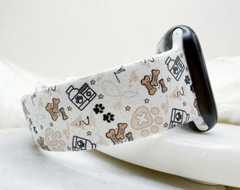 May include: A white silicone watch band featuring a repeating pattern of tan dog bones, black paw prints, black and white medicine bottles with paw print labels, and tan paw prints with white crosses, attached to a black watch connector.