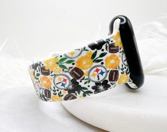 May include: A silicone watch band featuring a repeating pattern of yellow flowers, green leaves, brown footballs, and the Pittsburgh Steelers logo. The band is attached to a black watch connector, showcasing a vibrant, multi-colored sports-themed design.