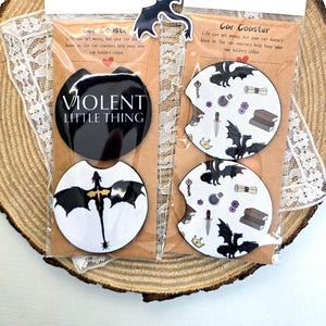 Peut inclure: Deux ensembles de dessous de verre de voiture noirs et blancs avec un motif de dragon. Un ensemble présente un dragon avec le texte "Violent Little Thing" et l'autre ensemble présente un dragon avec un motif de livres, de clés et d'un poignard.