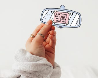 May include: A blue and white rearview mirror sticker with a pink note that reads "Don't look back, you're not going that way."