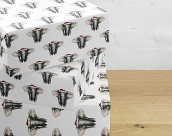 May include: Three white gift boxes with a repeating pattern of gray elephants wearing red Santa hats. The boxes are stacked on top of each other on a wooden surface.