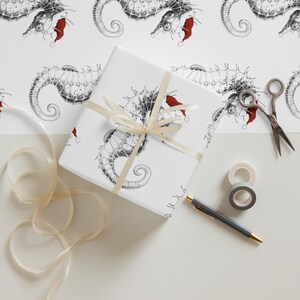 May include: A wrapped gift with seahorse illustrations wearing Santa hats, tied with a cream ribbon. The wrapping paper features a repeating pattern of black and white seahorses with red Santa hats. Scissors, tape, and a pen are nearby.
