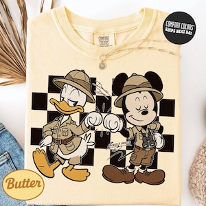 a yellow t-shirt with a cartoon illustration of two Disney characters, Mickey Mouse and Donald Duck, dressed in safari gear and standing next to each other.