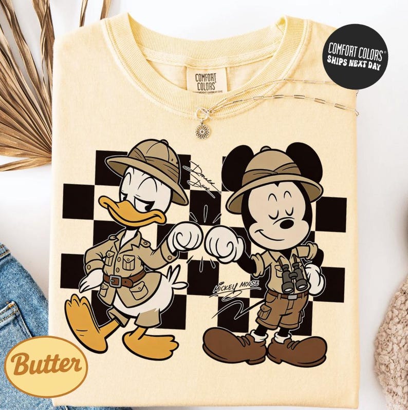 a yellow t-shirt with a cartoon illustration of two Disney characters, Mickey Mouse and Donald Duck, dressed in safari gear and standing next to each other.