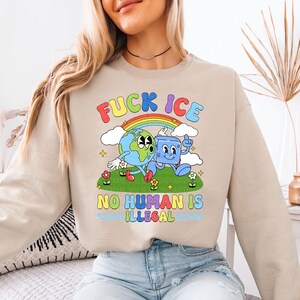 a woman sitting on a bed wearing a sweatshirt that says fucking ice no human is
