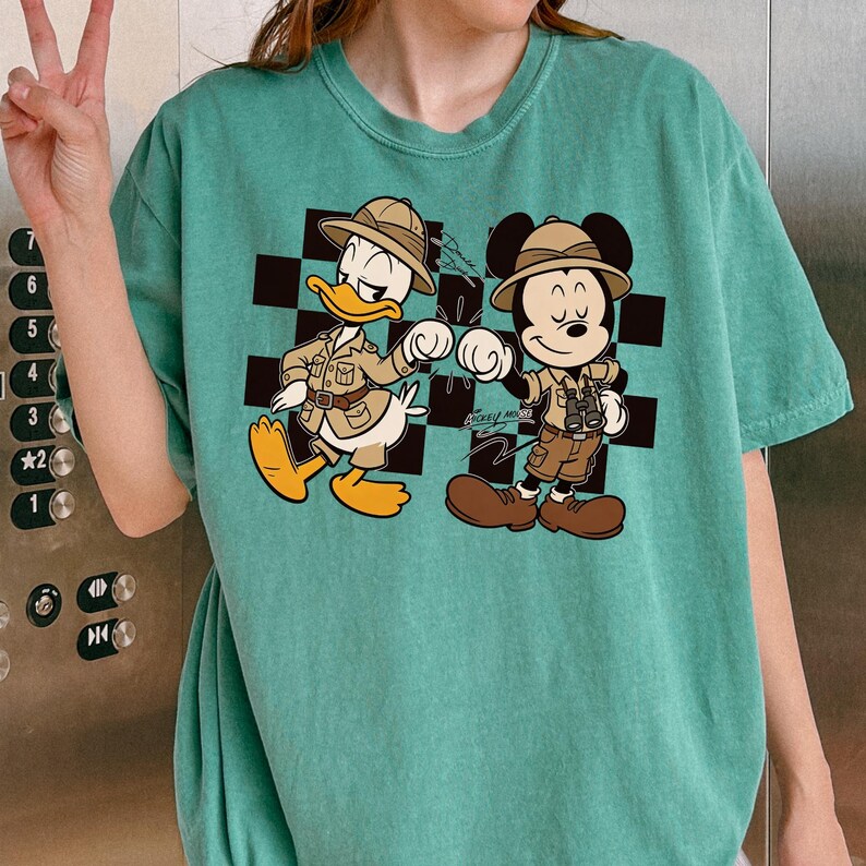 A person is wearing a green t-shirt with a cartoon image of Mickey Mouse and Donald Duck, who are depicted as adventurers or tourists.