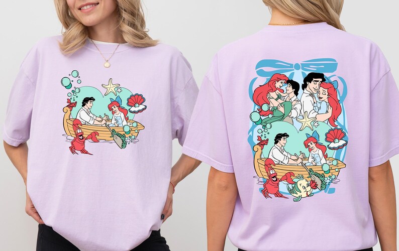 A woman wearing a pink t-shirt with a colorful graphic of characters from the Disney animated film "The Little Mermaid".