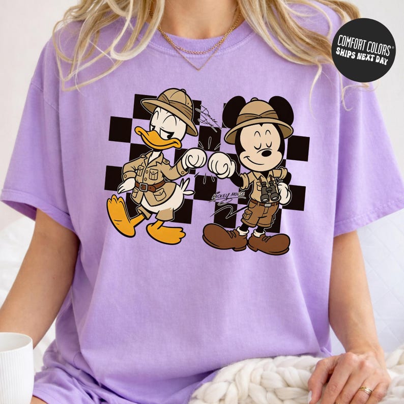 A person wearing a purple t-shirt with a cartoon image of Mickey Mouse and Donald Duck, who appear to be in a safari or adventure setting.