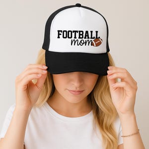 A woman wearing a black and white baseball cap with the text "FOOTBALL mom" on it.