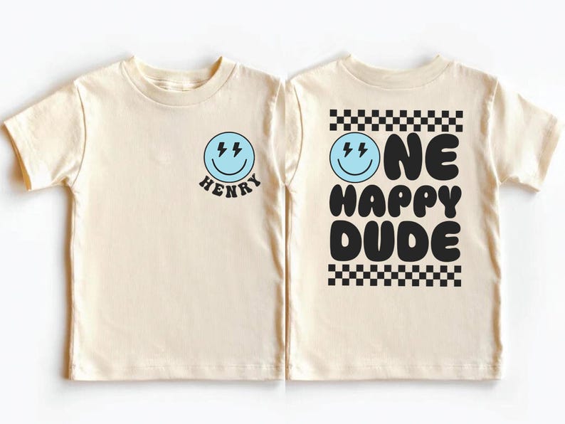 two white t-shirts with black text and graphics. The t-shirt on the left has a smiley face and the name "HENRY" below it, while the t-shirt on the right has the text "ONE HAPPY DUDE" and a checkered pattern.
