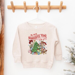 A white sweatshirt with a Christmas-themed graphic hanging on a wooden hanger.