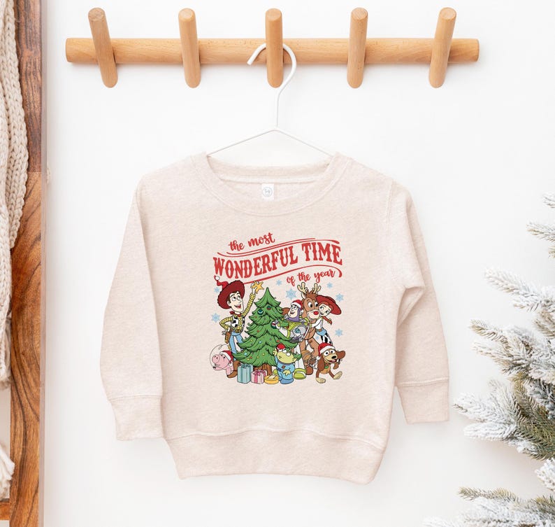 A white sweatshirt with a Christmas-themed graphic hanging on a wooden hanger.
