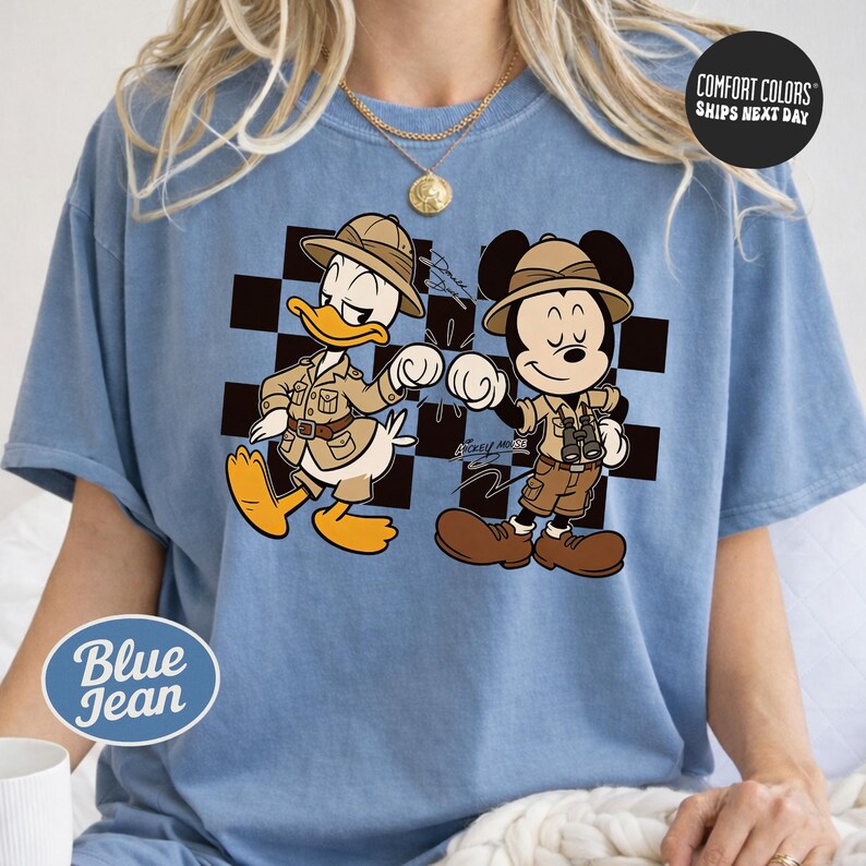 A blue t-shirt with a cartoon image of Mickey Mouse and Donald Duck, dressed in safari attire, standing next to each other.