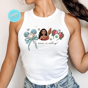 A woman wearing a white tank top with a graphic design featuring a cartoon character and text.