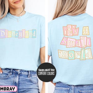 A woman wearing a light blue t-shirt with the text "Disneyland it's a small world" printed on it.