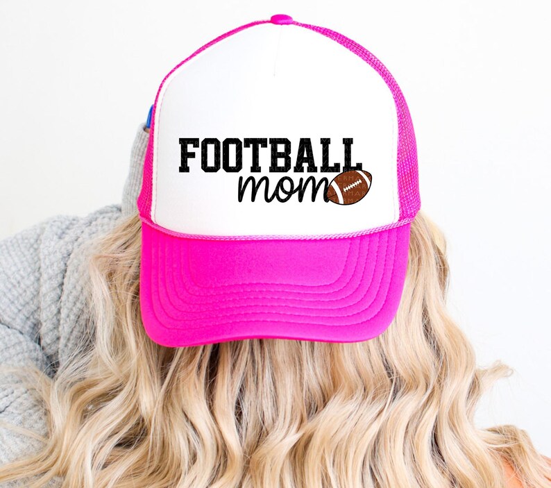 A person with blonde hair wearing a pink and white baseball cap with the text "FOOTBALL mom" printed on it.