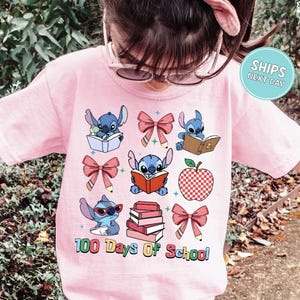 A young girl wearing a pink t-shirt with a graphic design featuring various cartoon characters and text related to school.