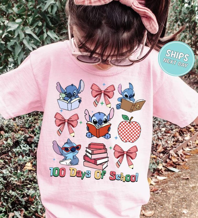 A young girl wearing a pink t-shirt with a graphic design featuring various cartoon characters and text related to school.