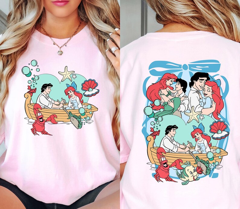 A woman wearing a pink t-shirt with a cartoon design of characters from the Disney film "The Little Mermaid".