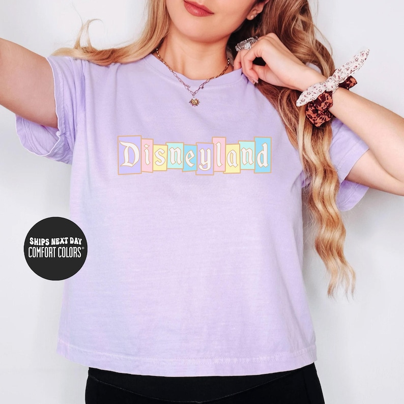 A woman wearing a purple t-shirt with the word "Disneyland" printed on it, posing with her arms outstretched.