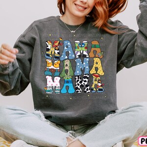 a woman sitting on a bed wearing a sweatshirt with letters on it