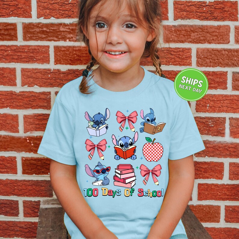 A young girl wearing a light blue t-shirt with a graphic design of various cartoon characters and text related to school.