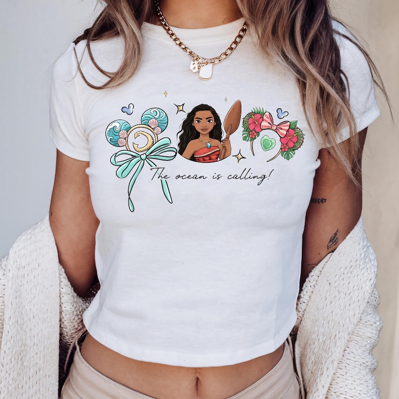 A woman wearing a white t-shirt with a graphic design featuring a cartoon character and the text "The ocean is calling!"