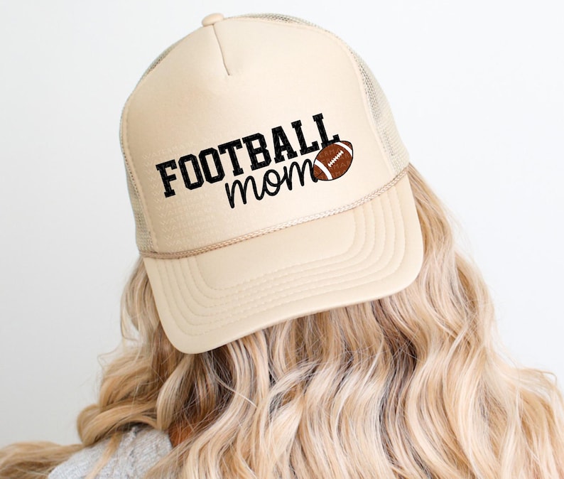 A person with long, wavy blonde hair wearing a beige baseball cap with the text "FOOTBALL mom" printed on it.