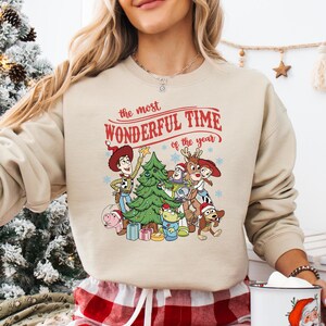 A woman wearing a beige sweater with a Christmas-themed graphic design featuring characters from the Toy Story franchise.