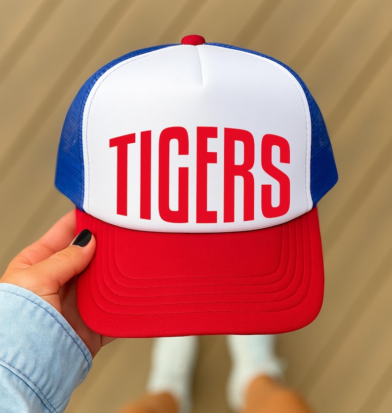 A person's hand holding a red and white baseball cap with the word "TIGERS" printed on it.