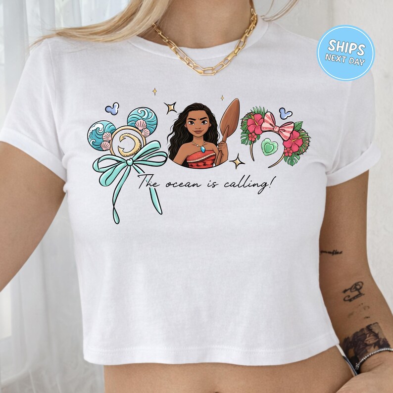 A white crop top with a graphic design featuring a woman surrounded by ocean-themed elements, including waves, flowers, and a ribbon.