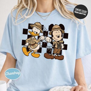 A woman wearing a light blue t-shirt with a cartoon image of two Disney characters, Mickey Mouse and Donald Duck, standing together.
