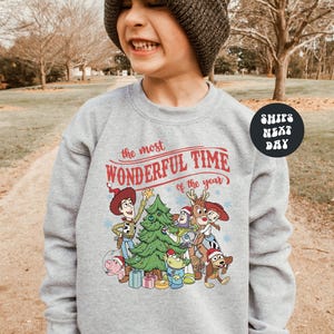 A young boy wearing a gray sweatshirt with a Christmas-themed graphic and text, smiling and looking at the camera.