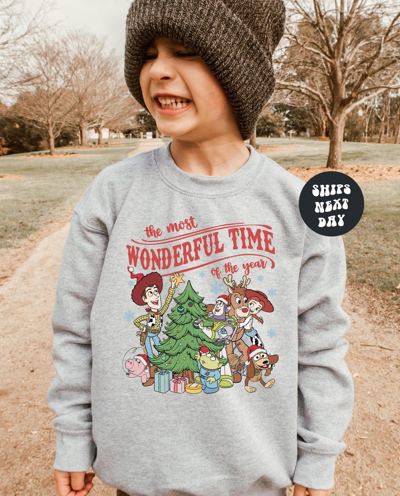 A young boy wearing a gray sweatshirt with a Christmas-themed graphic and text, smiling and looking at the camera.