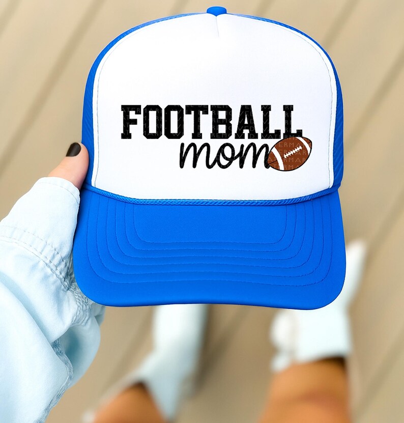 A person's hand holding a blue and white baseball cap with the text "FOOTBALL mom" printed on it.