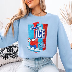 a woman sitting on a bed wearing a blue sweatshirt