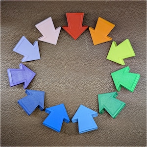 May include: A collection of twelve plastic arrow-shaped markers arranged in a circular pattern. The arrows feature a spectrum of colors including red, orange, lime green, emerald green, teal, light blue, royal blue, purple, lavender, and pink.