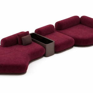 May include: Modular burgundy sofa set with rounded shapes. The set includes multiple seating sections, cylindrical backrests, and a built-in dark brown storage unit. The sofa is upholstered in a textured fabric.