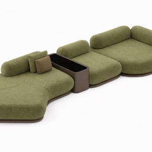 May include: A modular olive green sofa with rounded sections and a built-in dark brown storage unit. The sofa includes two cylindrical bolster pillows and two square pillows. The base of the sofa is a dark brown color.