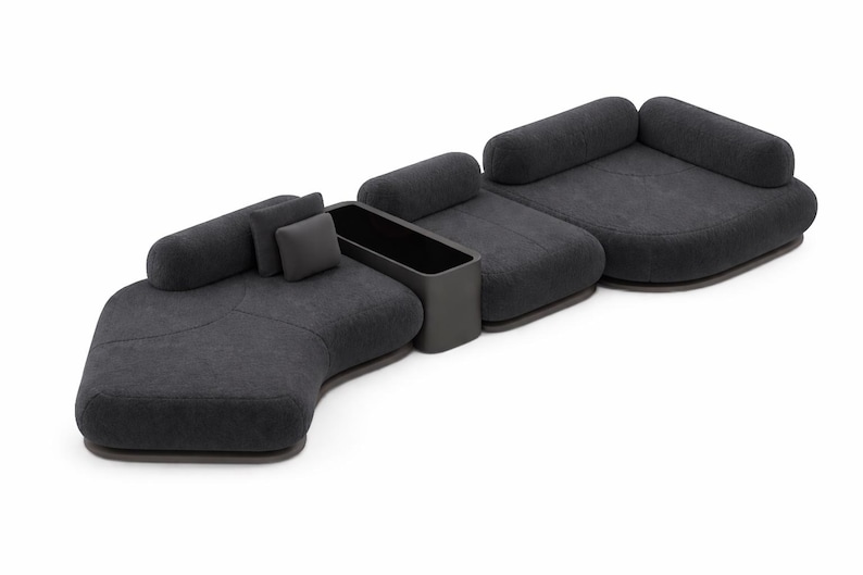 May include: Modular dark gray sofa with rounded shapes and a built-in storage unit. The sofa has several sections, including a curved chaise lounge, a loveseat, and a single seat, all with soft, textured upholstery. Includes two cylindrical and one square pillow.