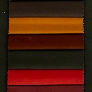 May include: A vertical swatch card featuring a variety of fabric samples in shades of beige, brown, red, and blue. The samples are arranged in horizontal rows, showcasing different textures and colors, ideal for upholstery or interior design projects.